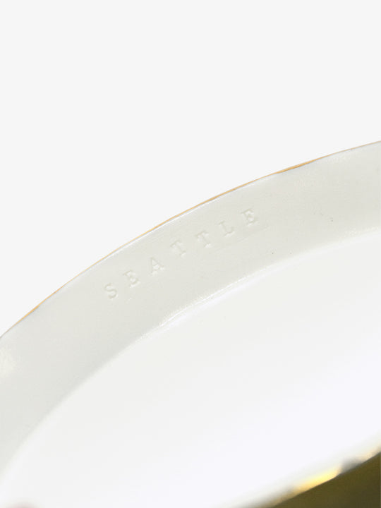 Detail of JINJIN PARIS Golden Rim Shallow Plate Medium with subtle “SEATTLE” embossing along the interior rim.
