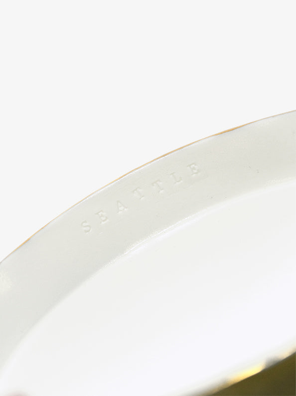 Detail of JINJIN PARIS Golden Rim Shallow Plate Medium with subtle “SEATTLE” embossing along the interior rim.