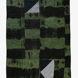 Back view of hand-dyed patchwork quilt by Lily Raskind in green and black tones with abstract panel layout, shown flat.