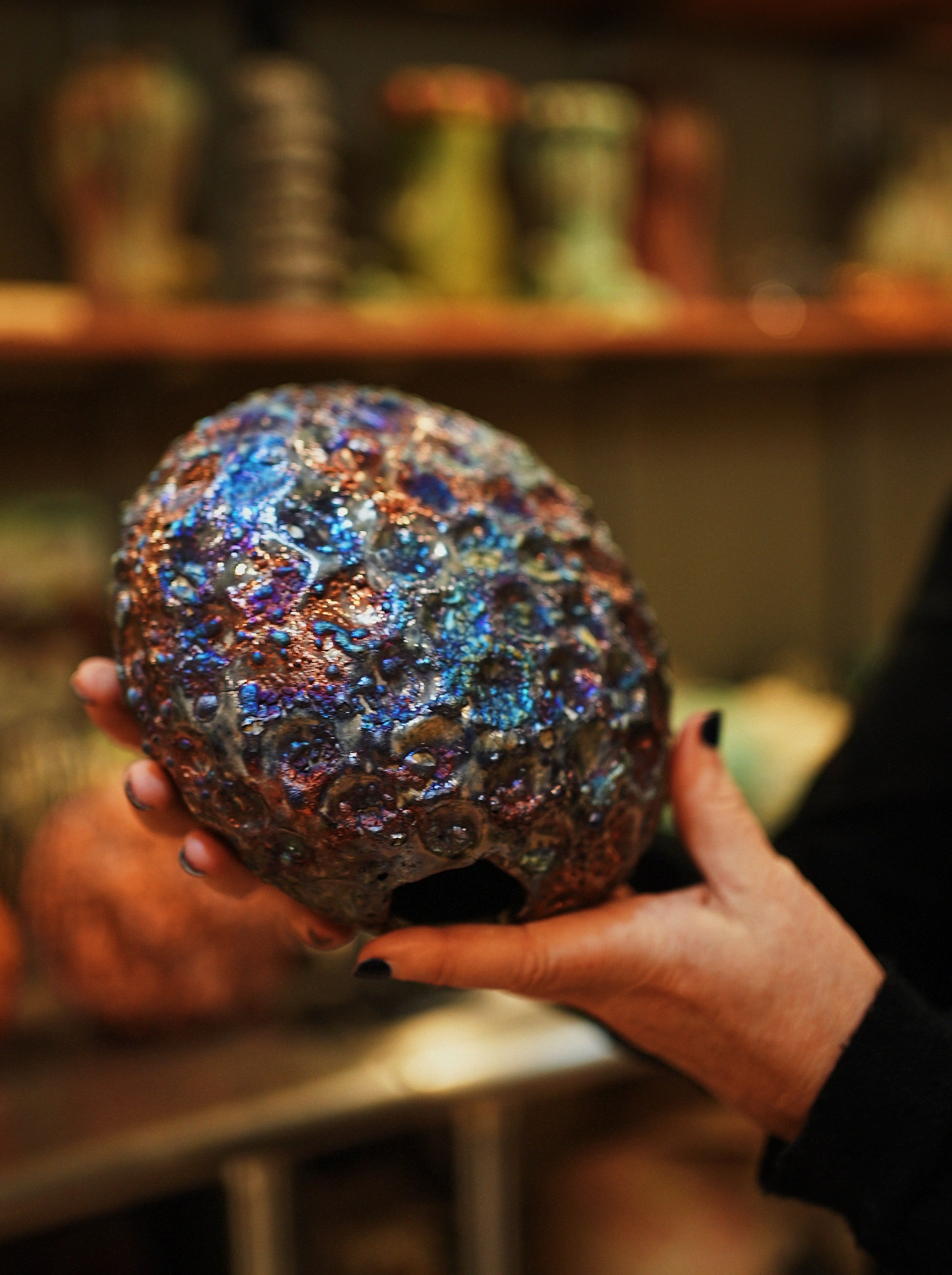 Ann Shure holding an iridescent raku-fired ceramic piece resembling vesicular basalt rock