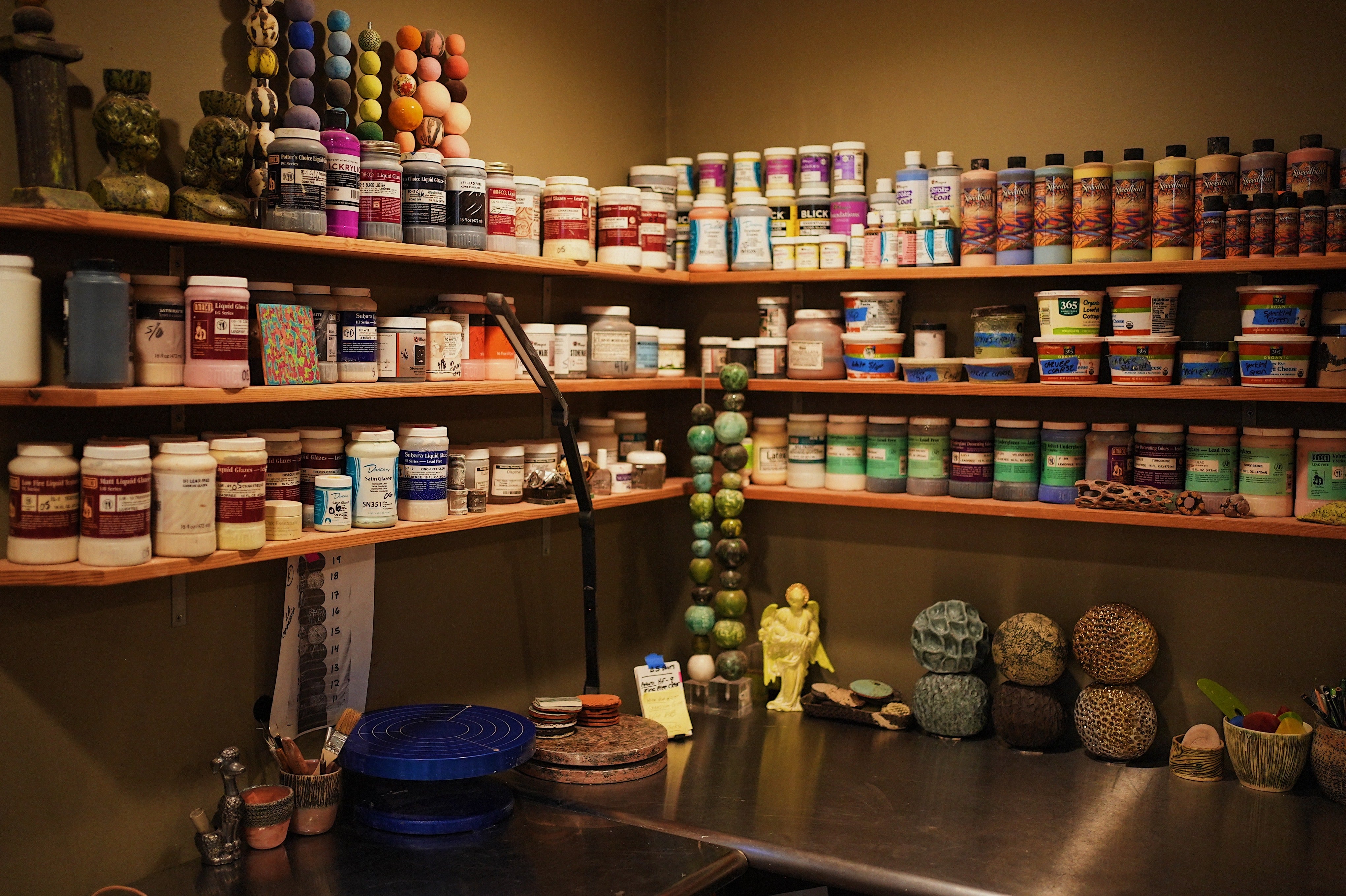 Corner of Ann Shure’s studio with shelves of supplies, paints, mock-up sculptures, and ceramic works on desk