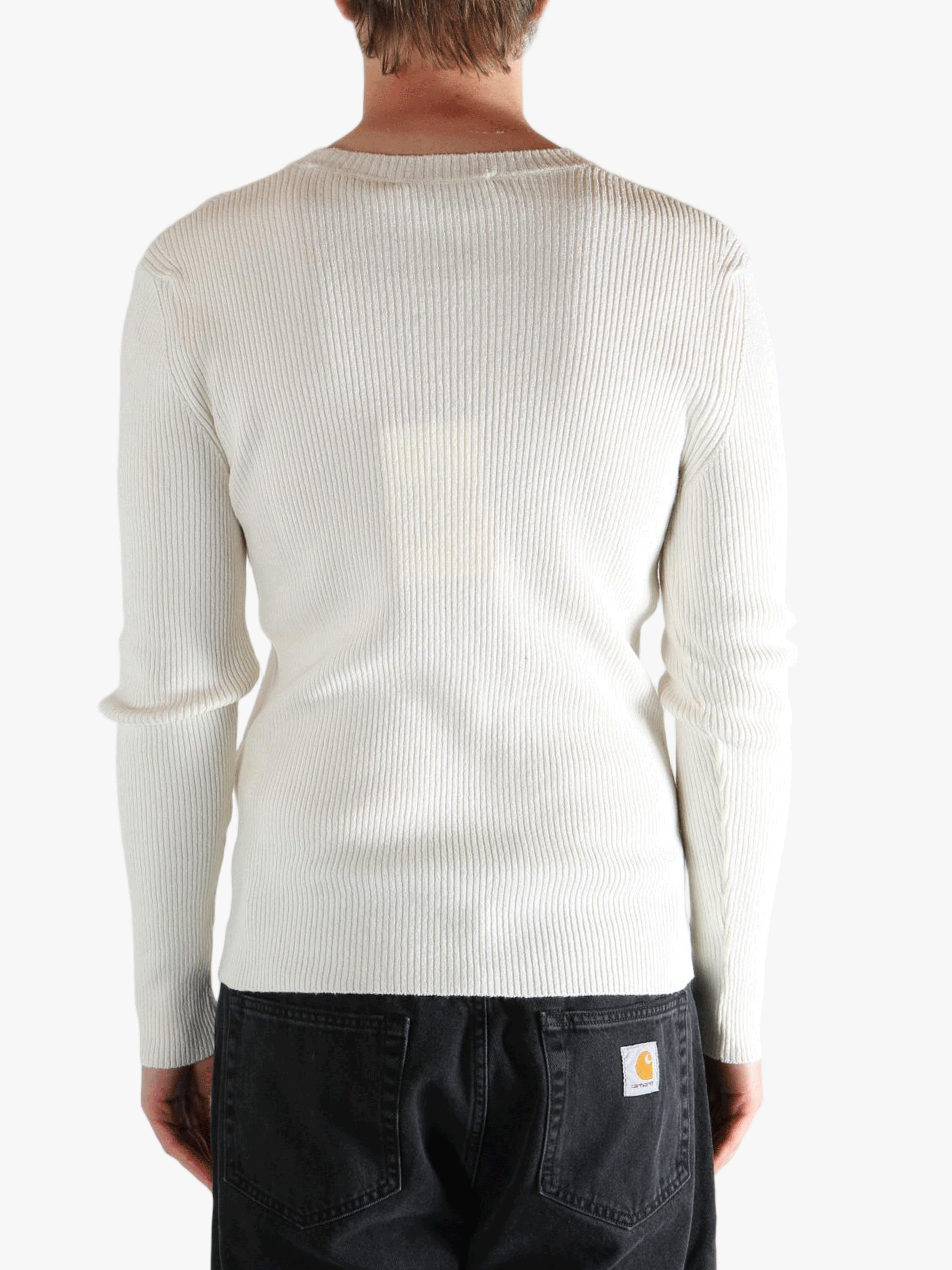 Person wearing a beige ribbed sweater and black pants on a white background