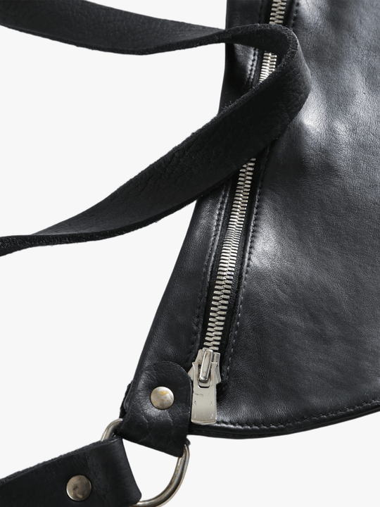 Close-up of a black leather bag with a zipper and strap details on a white background