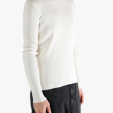 Person wearing a beige ribbed sweater and black pants on a white background