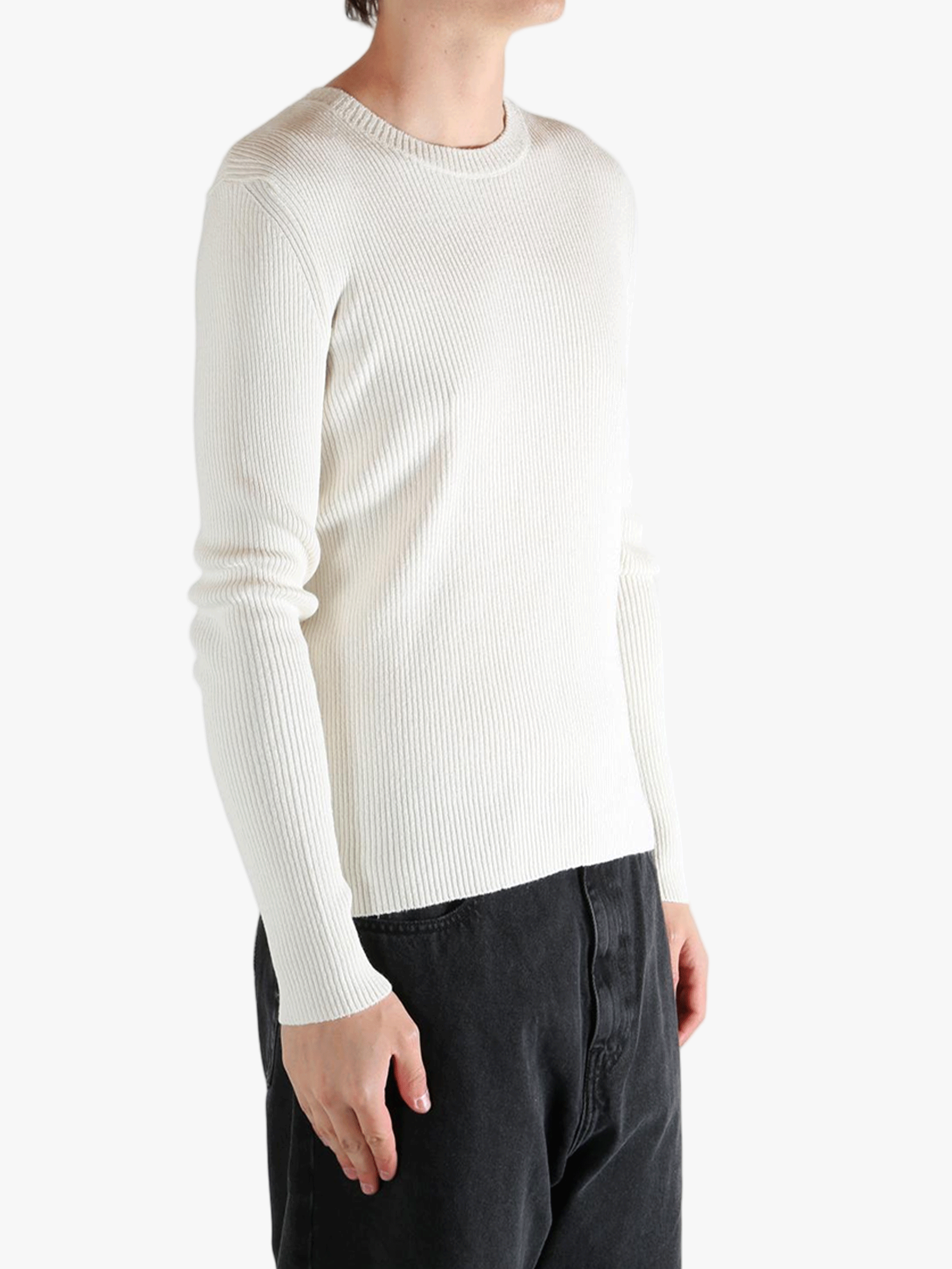 Person wearing a beige ribbed sweater and black pants on a white background