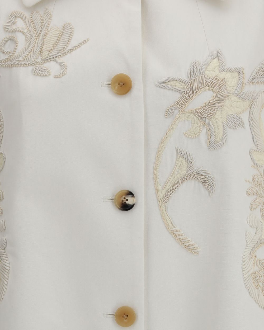 Close-up of a white garment with floral embroidery and buttons