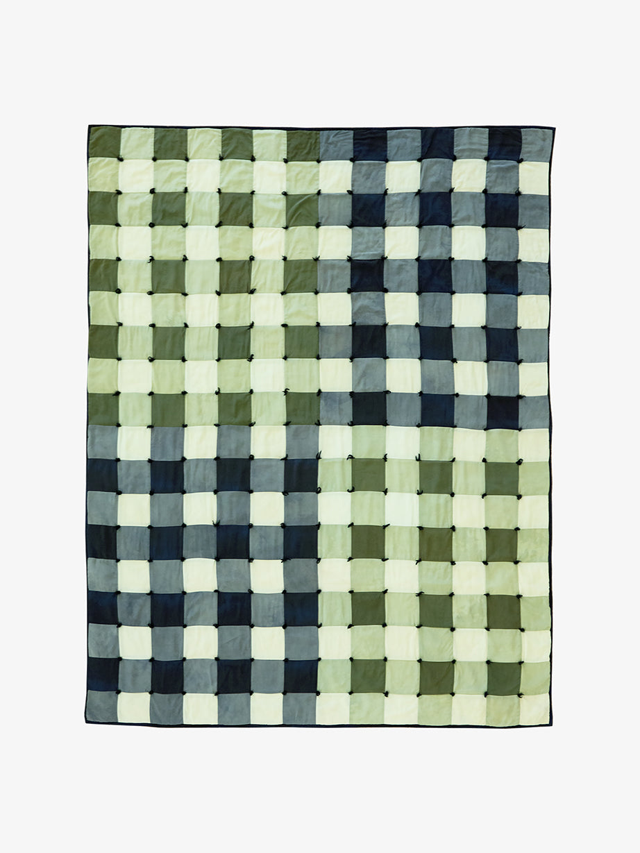 Woven checkered quilt with green, blue, and white squares on a white background