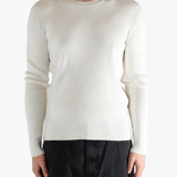 Person wearing a beige ribbed sweater and black pants on a white background
