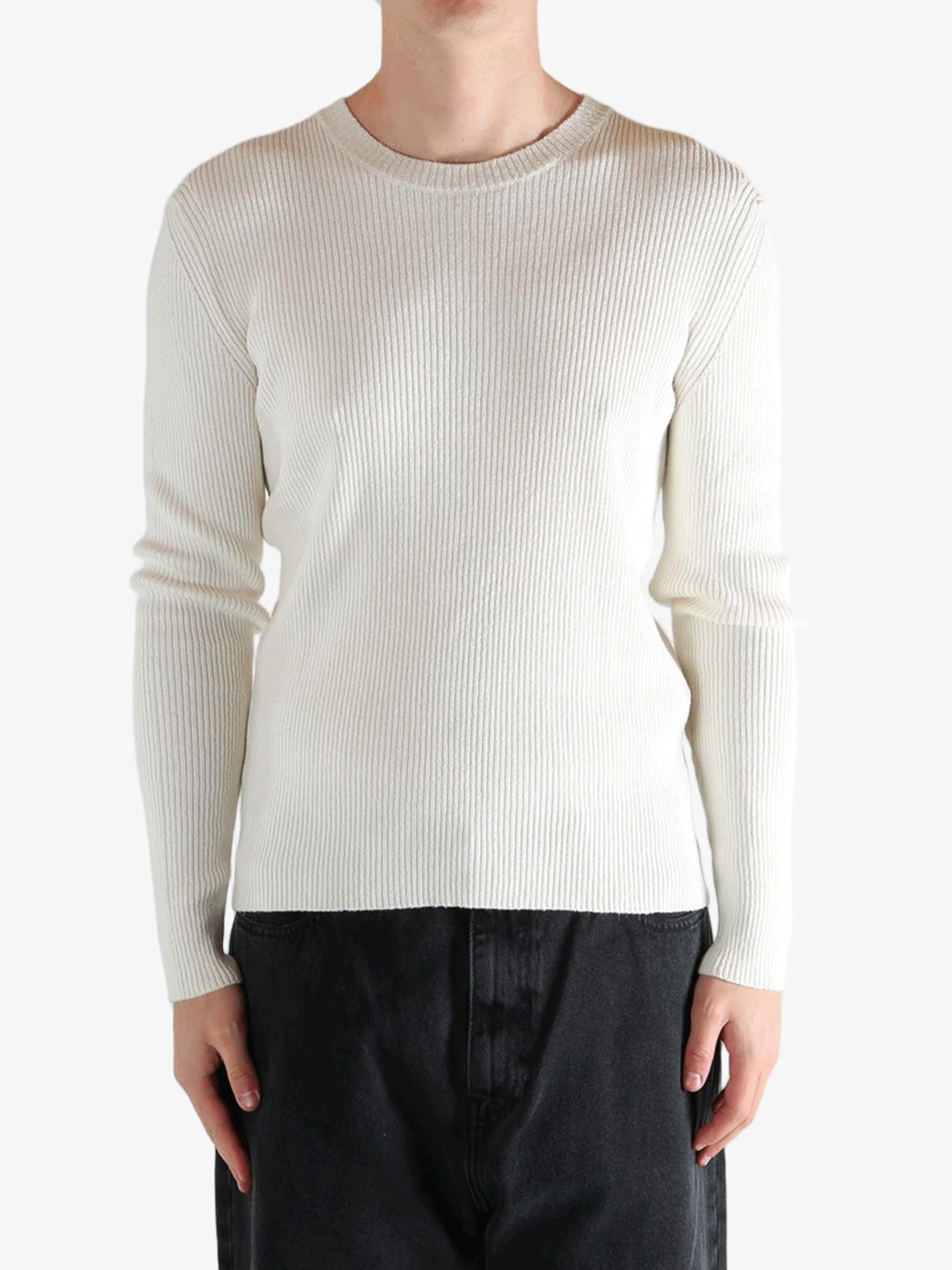 Person wearing a beige ribbed sweater and black pants on a white background