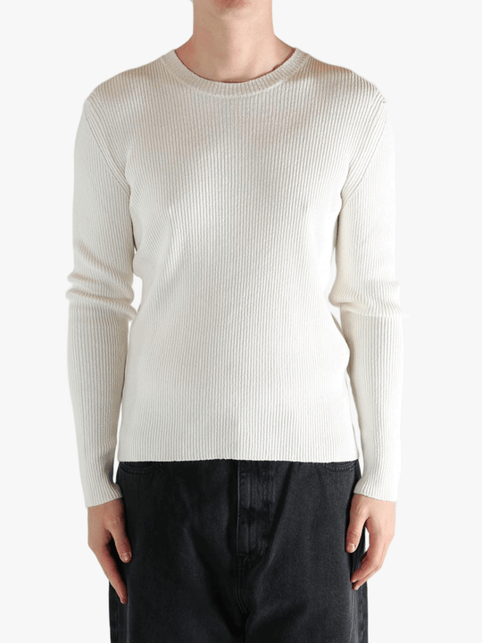 Person wearing a beige ribbed sweater and black pants on a white background