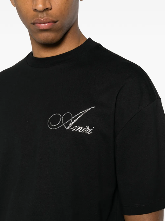 Black t-shirt with 'Amiri' logo worn by a person on a white background